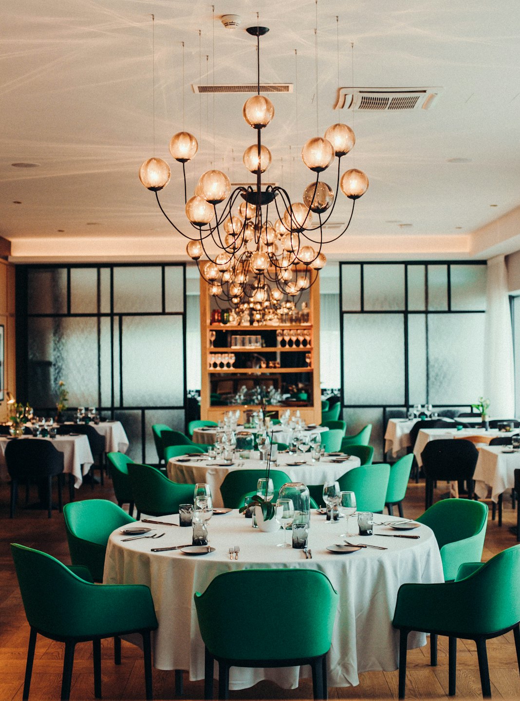 Elegant restaurant dining room with round tables and green chairs.