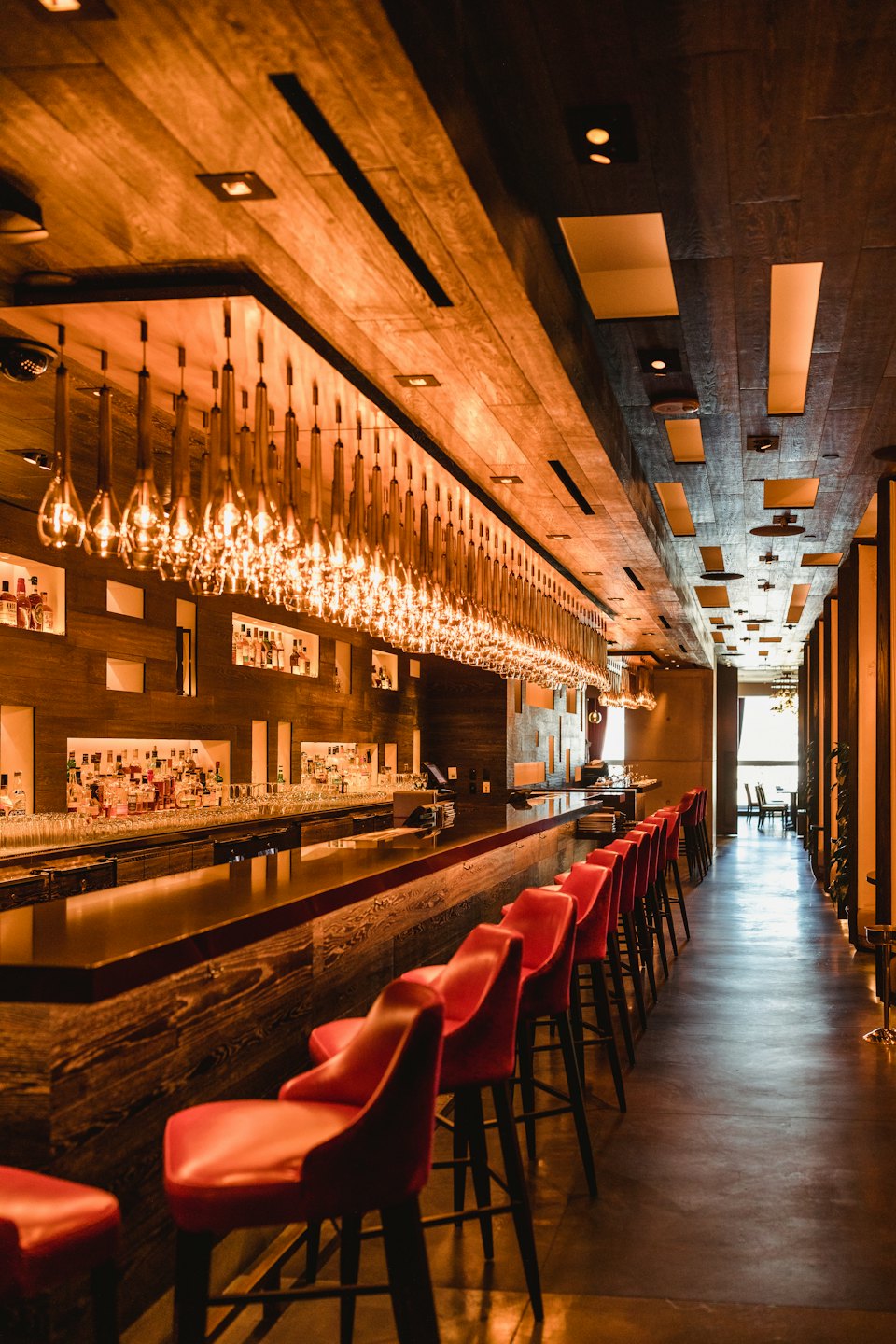 Modern bar with red stools lining a wooden counter.
